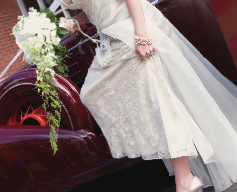 A bride stepping from a vintage burgundy car with her bouquet