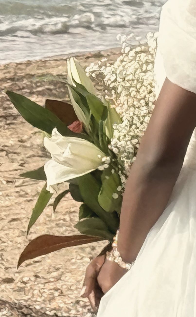 White lilies held behind a bride’s back on the beach