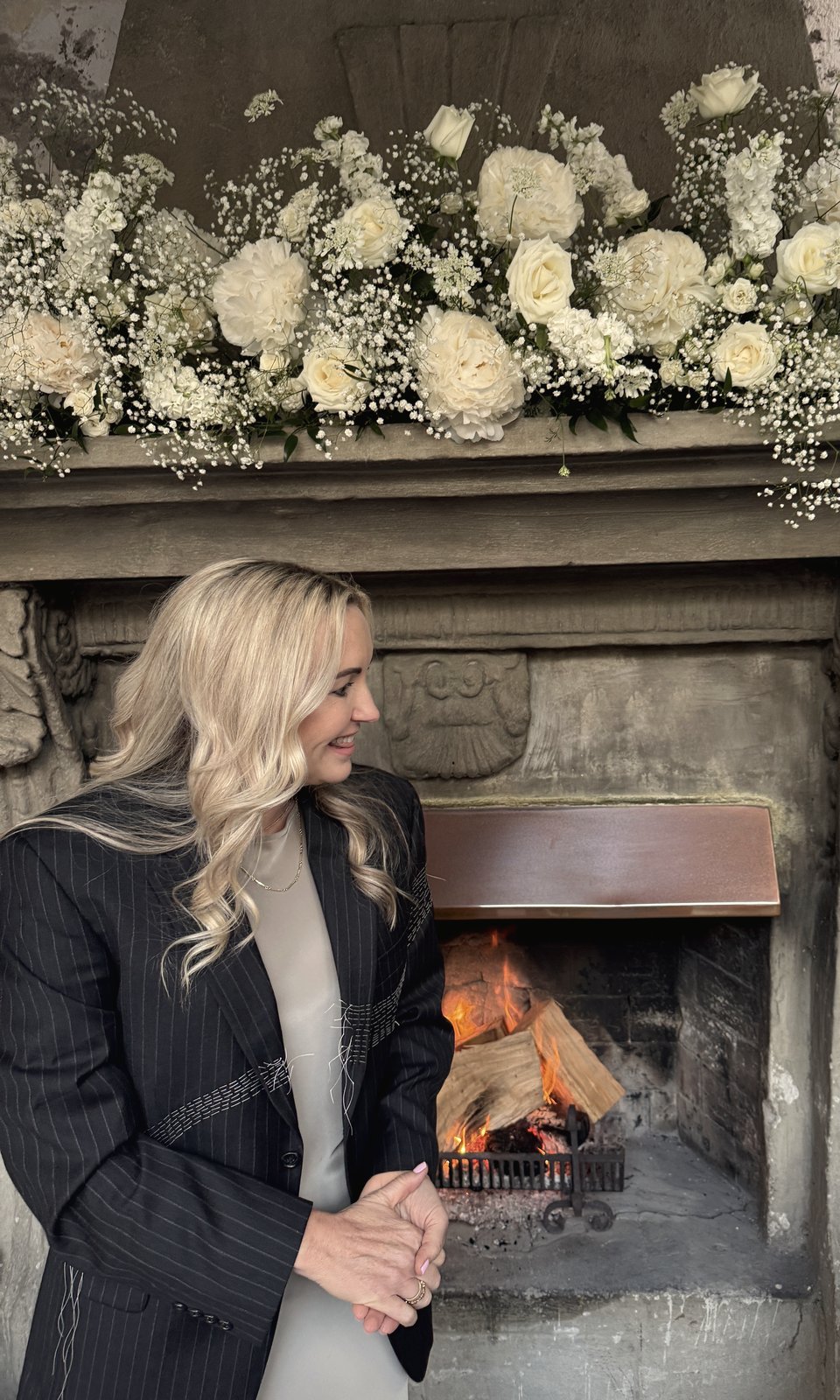 Lizzi beside a fireplace dressed with white flowers at a ceremony