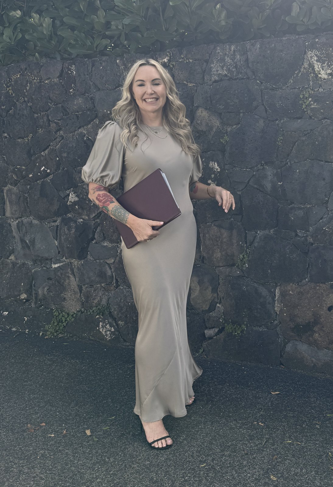 Lizzi smiling in front of a stone wall, holding her ceremony folder